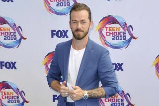 Artem Chigvintsev posing in a blue blazer, a white t-shirt and a watch against a white background with blue text 