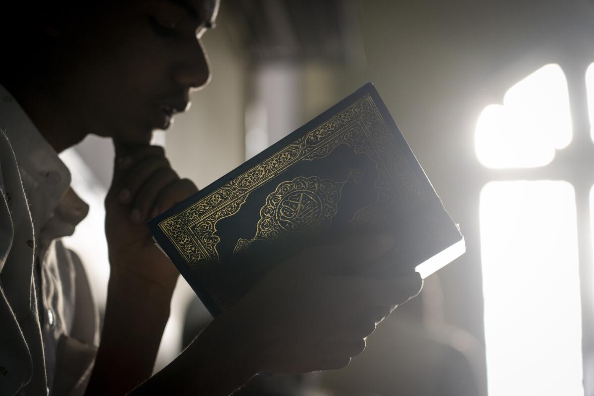 A Nepalese Muslim recites the Quran amid filtered light in a mosque.