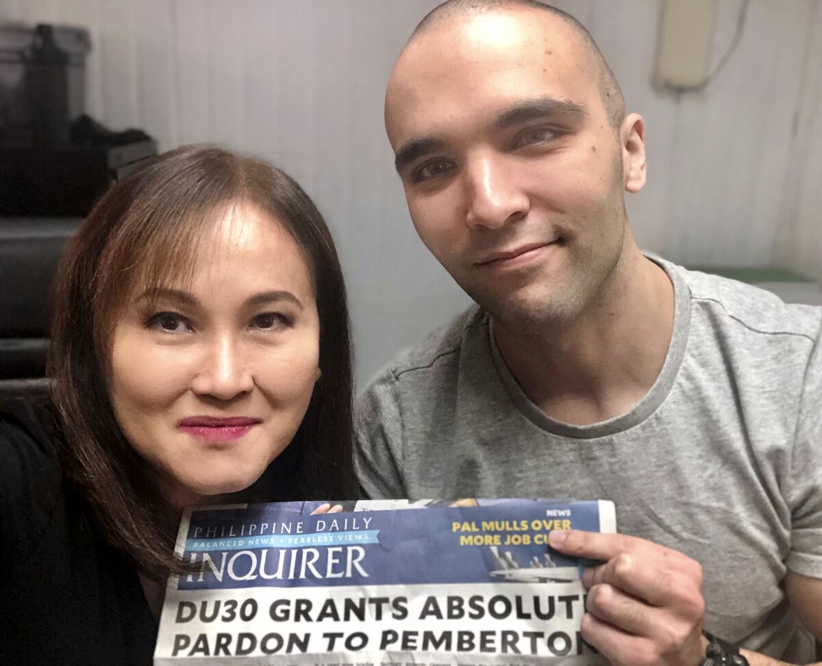 In this photo provided by Atty. Rowena Garcia-Flores, U.S. Marine Lance Cpl. Joseph Scott Pemberton, right, poses for a selfie while showing the headlines of a newspaper beside his lawyer Rowena Garcia-Flores on Tuesday Sept. 8, 2020 in Camp Aguinaldo, Quezon city, Philippines. The Philippine president recently pardoned Pemberton in a surprise move that will free him from imprisonment in the 2014 killing of a transgender Filipino woman that sparked anger in the former American colony. (Atty. Rowena Garcia-Flores via AP)