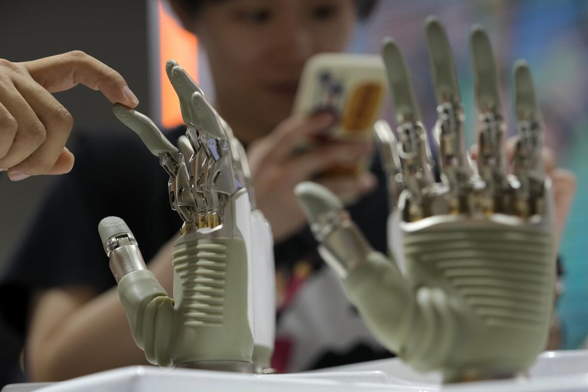 A human hand touching a finger of one of two robotic hands.