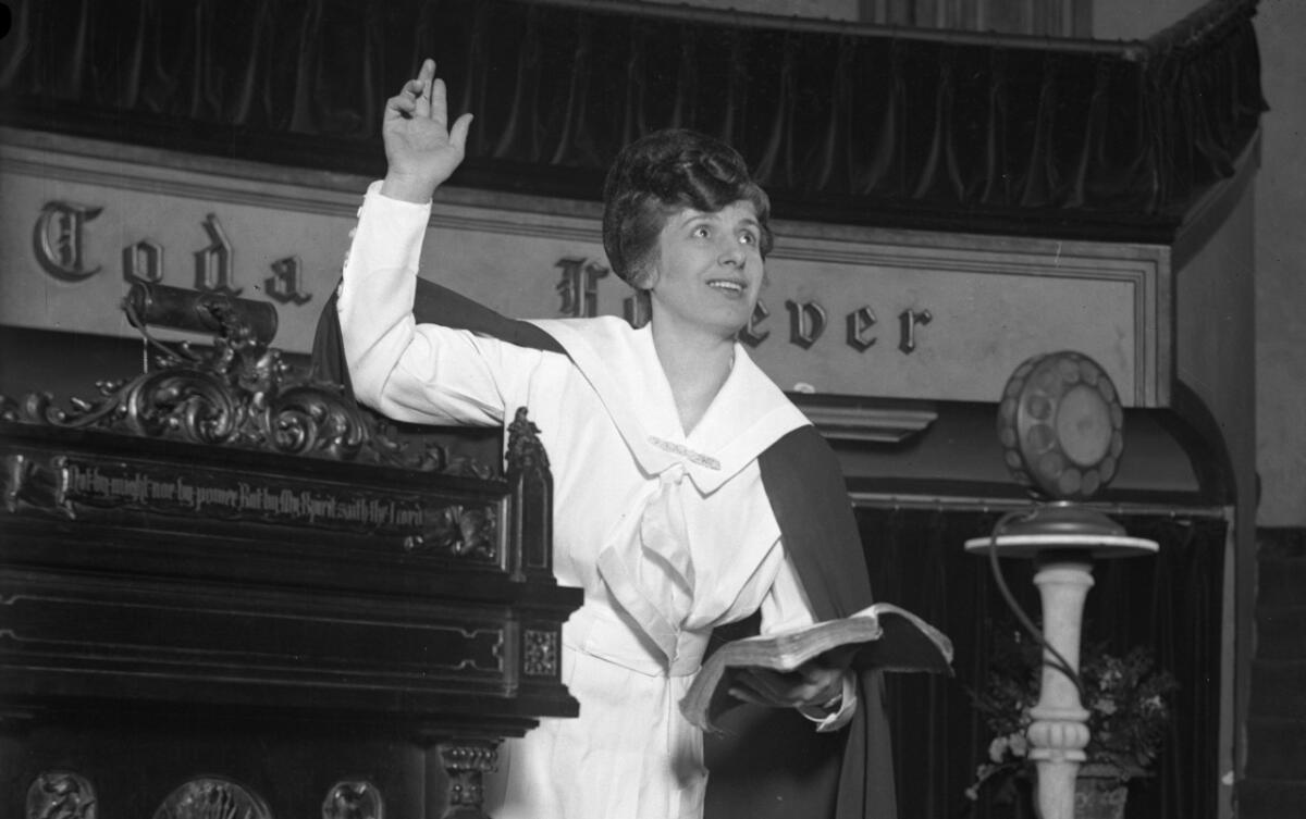 A woman in white holds a Bible in her left hand as she extends her other hand toward the ceiling.