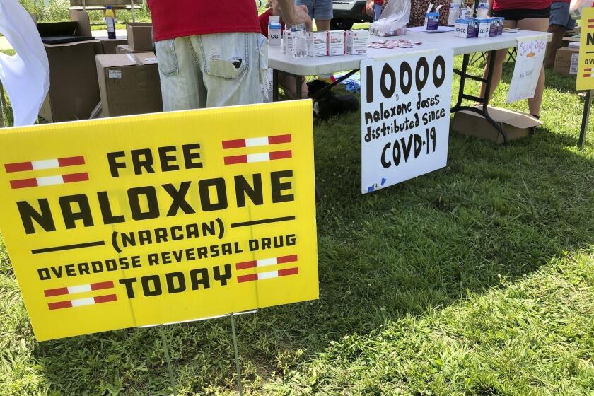 FILE - Signs are displayed at a tent during a health event on June 26, 2021, in Charleston, W.Va. Volunteers at the tent passed free doses of naloxone, a drug that reverses the effects of an opioid overdose by helping the person breathe again. The U.S. needs a more nimble strategy and Cabinet-level leadership to counter its festering opioid epidemic, a bipartisan congressional commission said Tuesday. (AP Photo/John Raby, File)