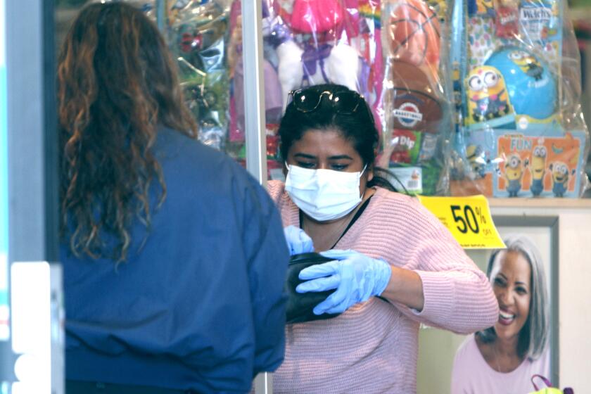 A shopper is seen from outside the store wearing mask and gloves while paying at Rite Aid, on Foothill Blvd. in La Canada Flintridge on Tuesday, April 14, 2020.