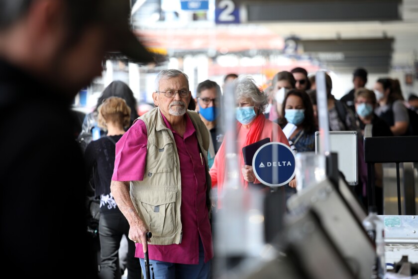 An unmasked man using a cane stands in a line of people wearing masks at an airline counter.