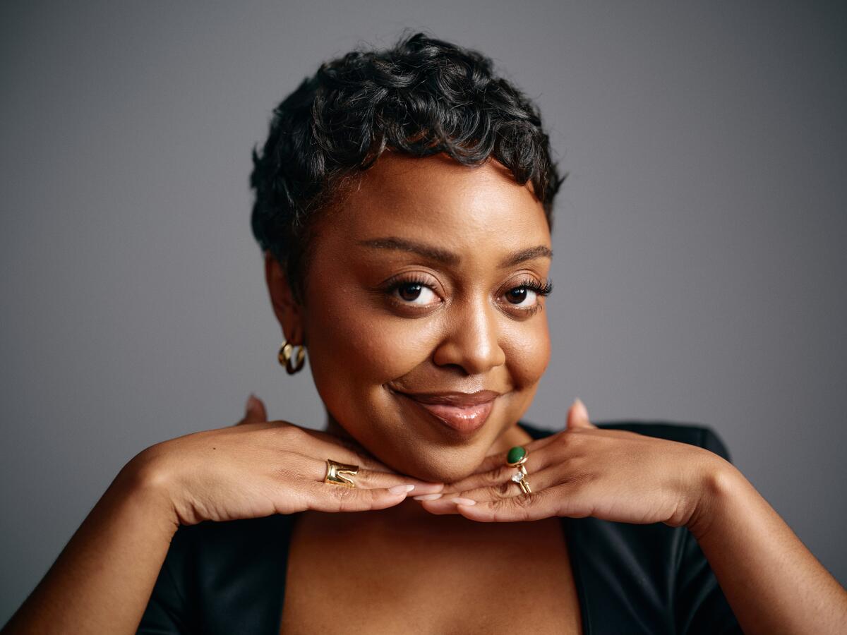 Quinta Brunson in a black dress smiles with her hands under her chin