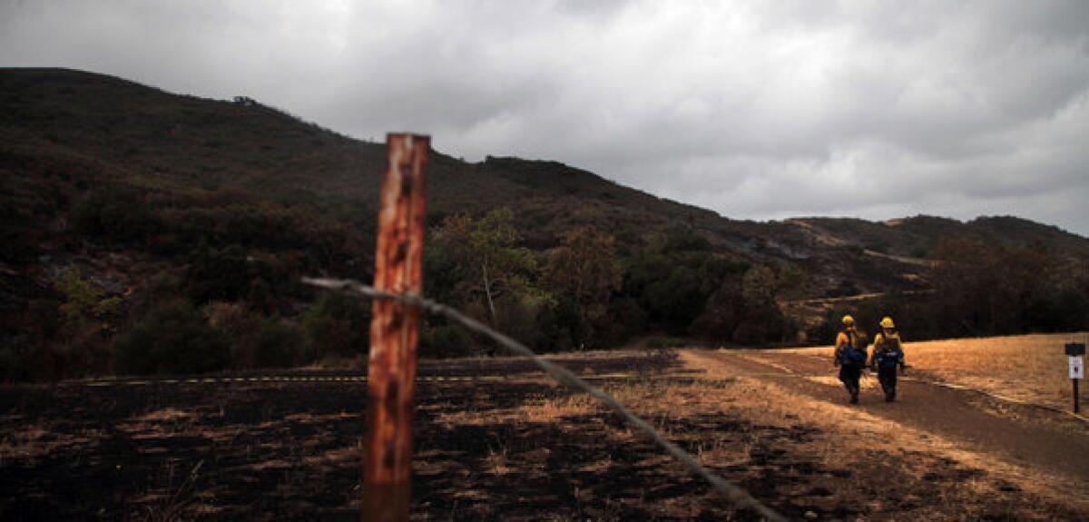 With the Springs fire in Ventura County reported 60% contained as of Sunday morning, firefighters walk through a burned-out area of Newbury Park.