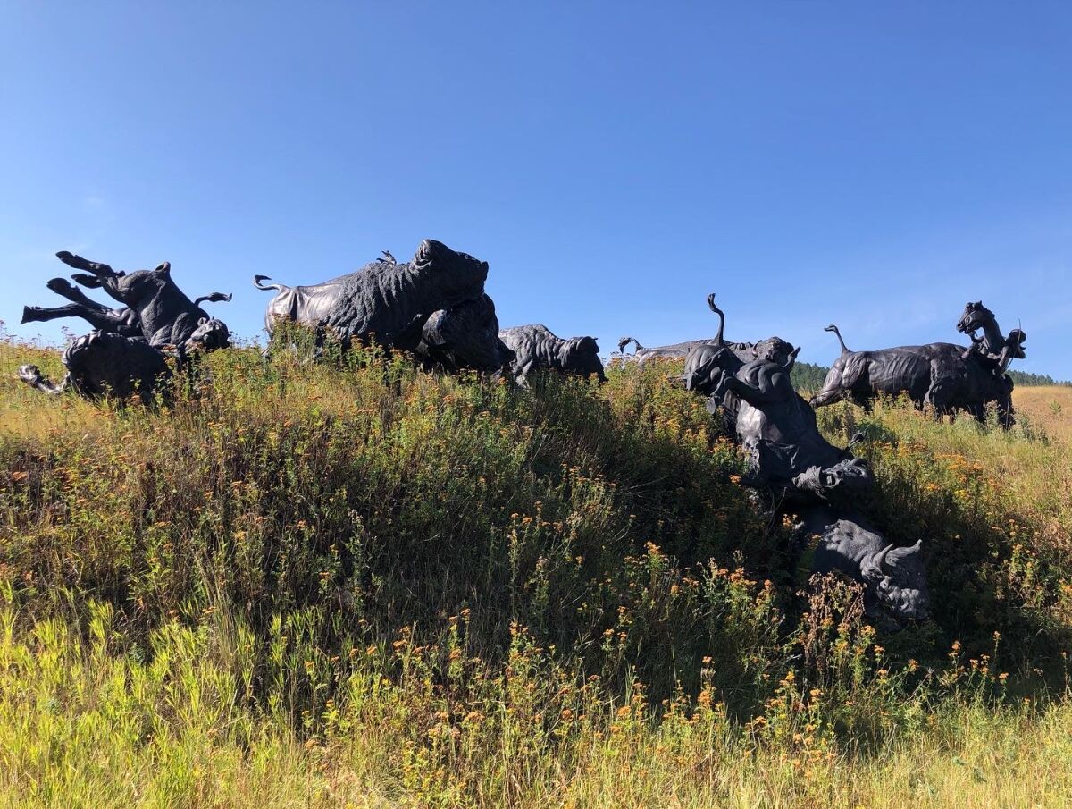 A bronze sculpture showing bison being pursued by Lakota riders amid a grassy area