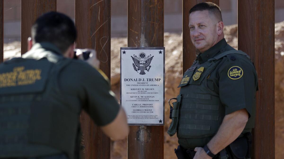 A Border Patrol agent poses next to plaque proclaiming a section of border fence in Calexico, Calif., the "first section of President Trump's border wall."