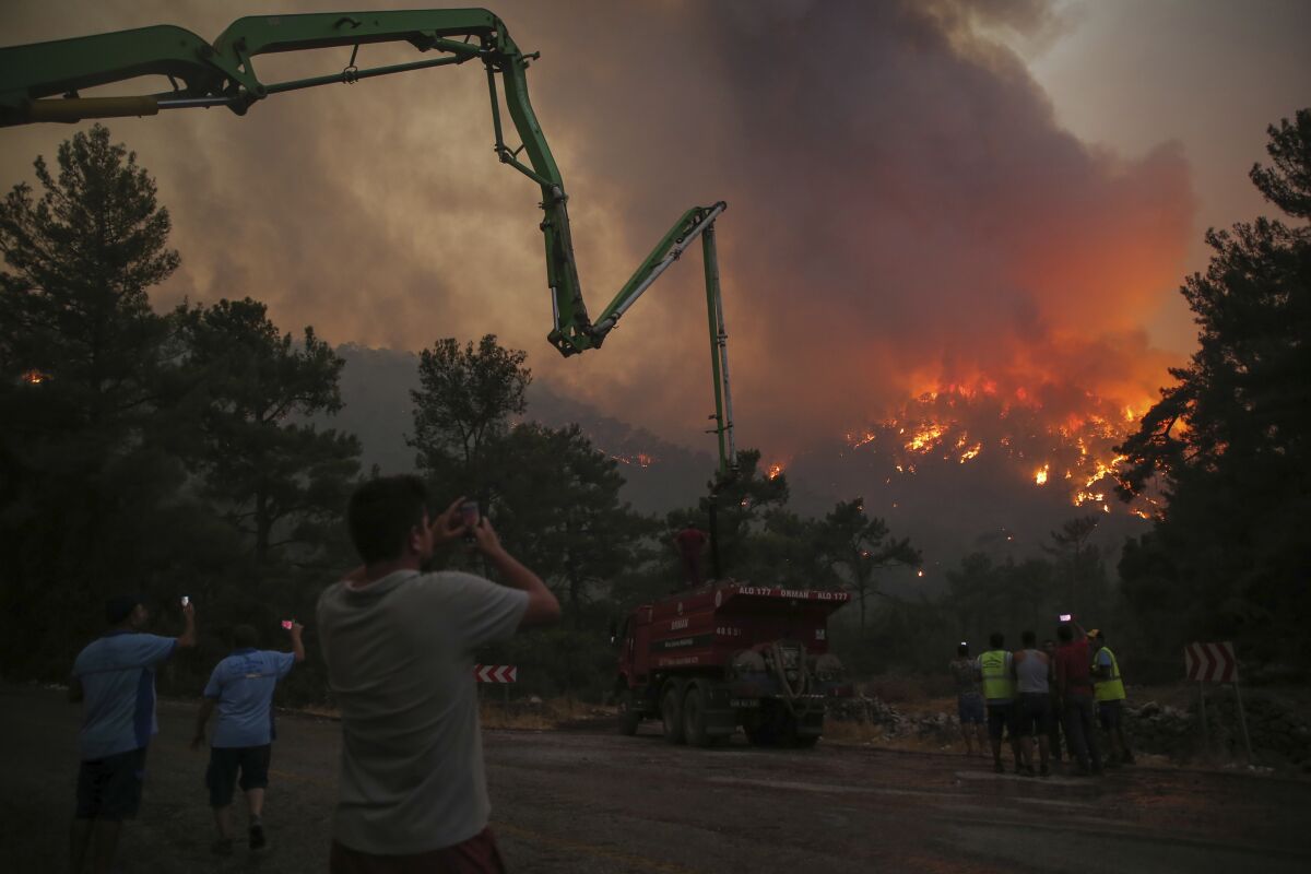 People watch an advancing fire that rages Cokertme village, near Bodrum, Turkey, Monday, Aug. 2, 2021. For the sixth straight day, Turkish firefighters battled Monday to control the blazes that are tearing through forests near Turkey's beach destinations. Fed by strong winds and scorching temperatures, the fires that began Wednesday have left eight people dead. Residents and tourists have fled vacation resorts in flotillas of small boats or convoys of cars and trucks. (AP Photo/Emre Tazegul)