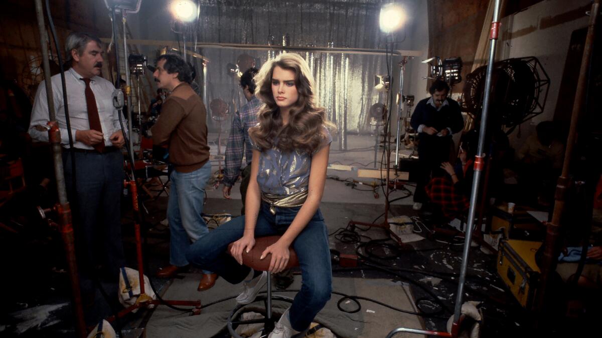 A young Brooke Shields on a movie set surrounded by lights and two male crew members.