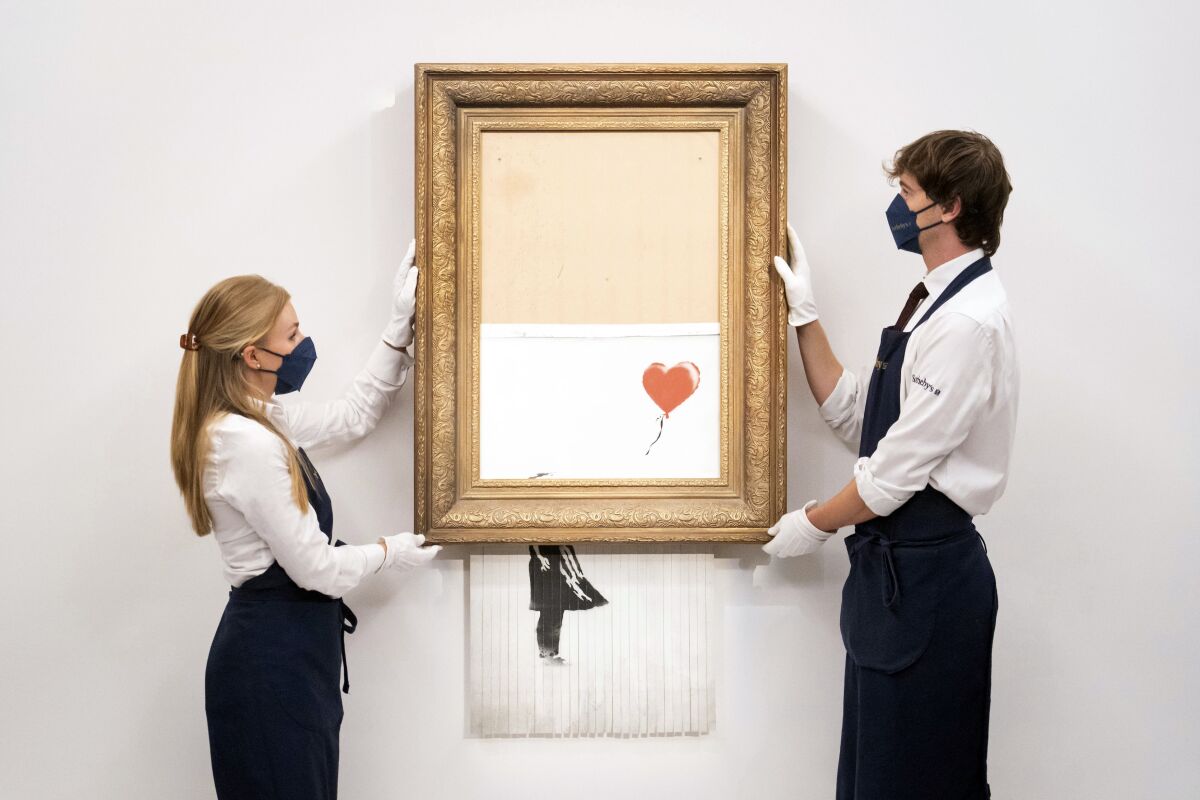 Art handlers at Sotheby's auction house hold Banksy's 'Love is in the Bin', before it returns to auction at Sotheby's, London, Friday, Sept. 3, 2021. A Banksy artwork that was sensationally shredded just after it sold for $1.4 million us up for sale again -- at several times the price. Sotheby’s said Friday that “Love is in the Bin” will be offered at an Oct. 14 auction in London, with a pre-sale estimate of 4 million pounds to 6 million pounds ($5.5 million to $8.3 million). (Dominic Lipinski/PA via AP)