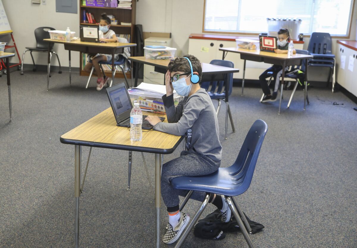 Steven Gortani, 6, and other children work on their laptops with several feet of space separating the desks.