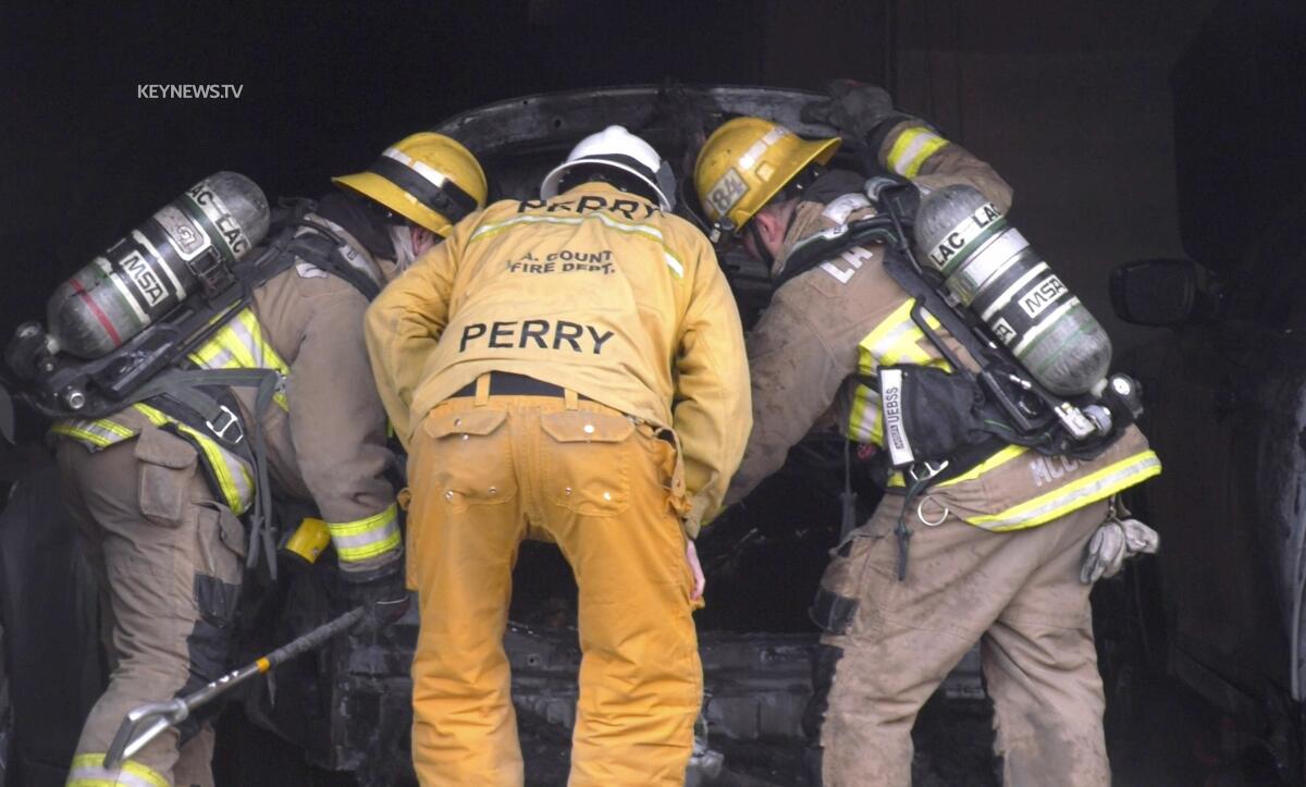Three firefighters look into a car trunk after a fire.