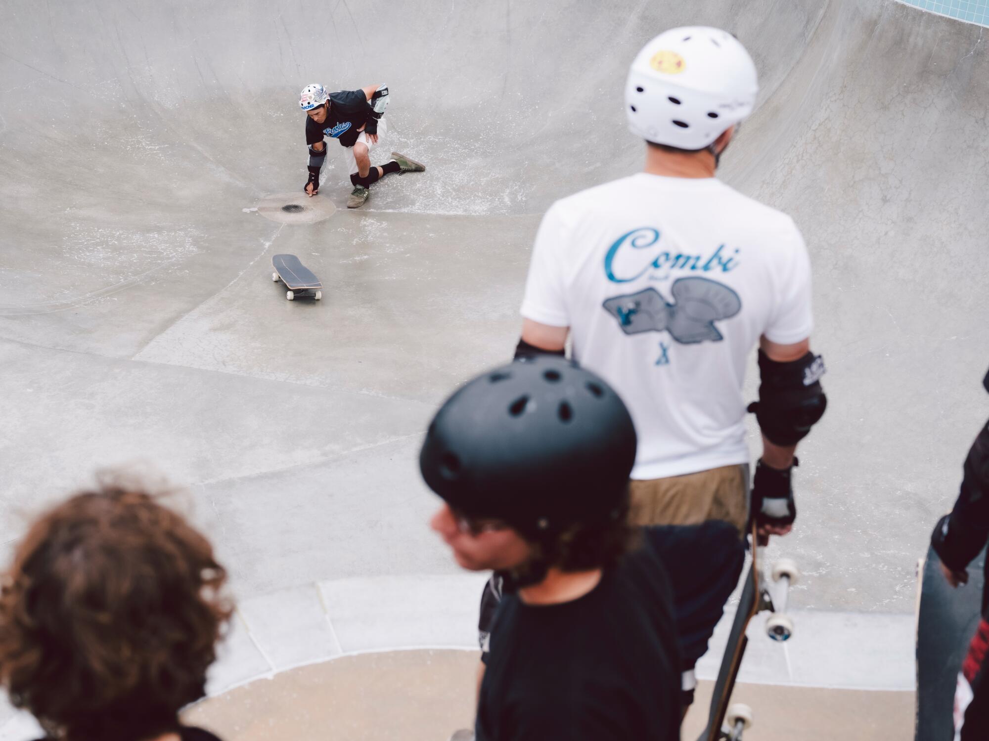 A skateboarder wipes out as others watch on.