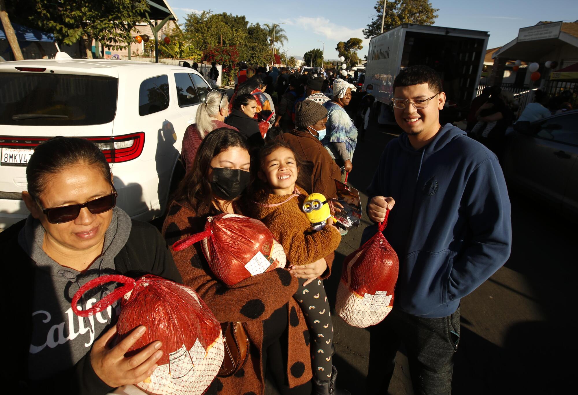 A row of people hold wrapped turkeys.