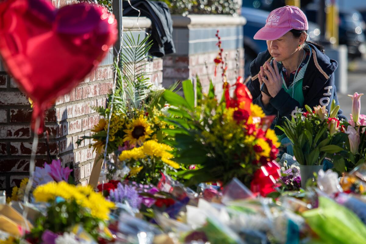 A woman clasps her hands while kneeling in front of a makeshift memorial.