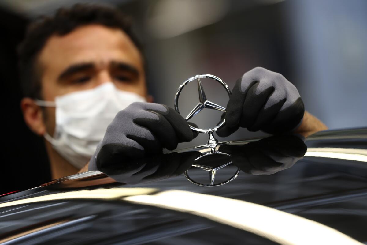 A masked worker attaches a Mercedes emblem