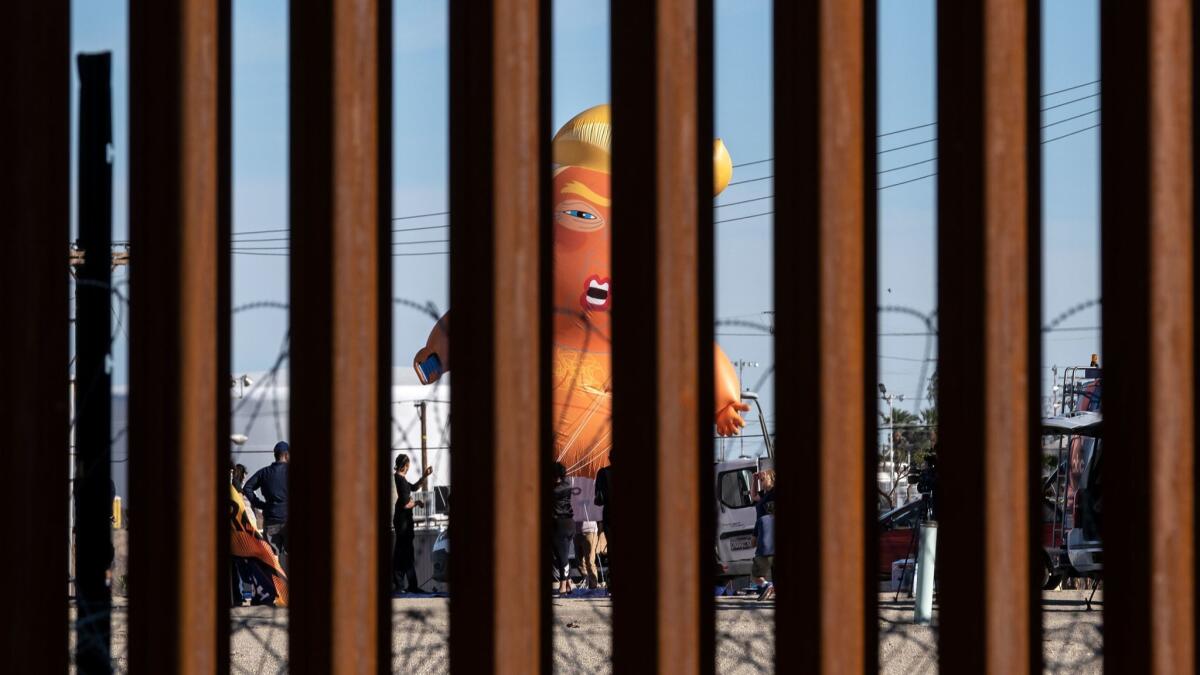 A satirical balloon of a baby US President Donald Trump is seen through the US-Mexico border fence during a demonstration against him prior to his visit to Calexico, California.