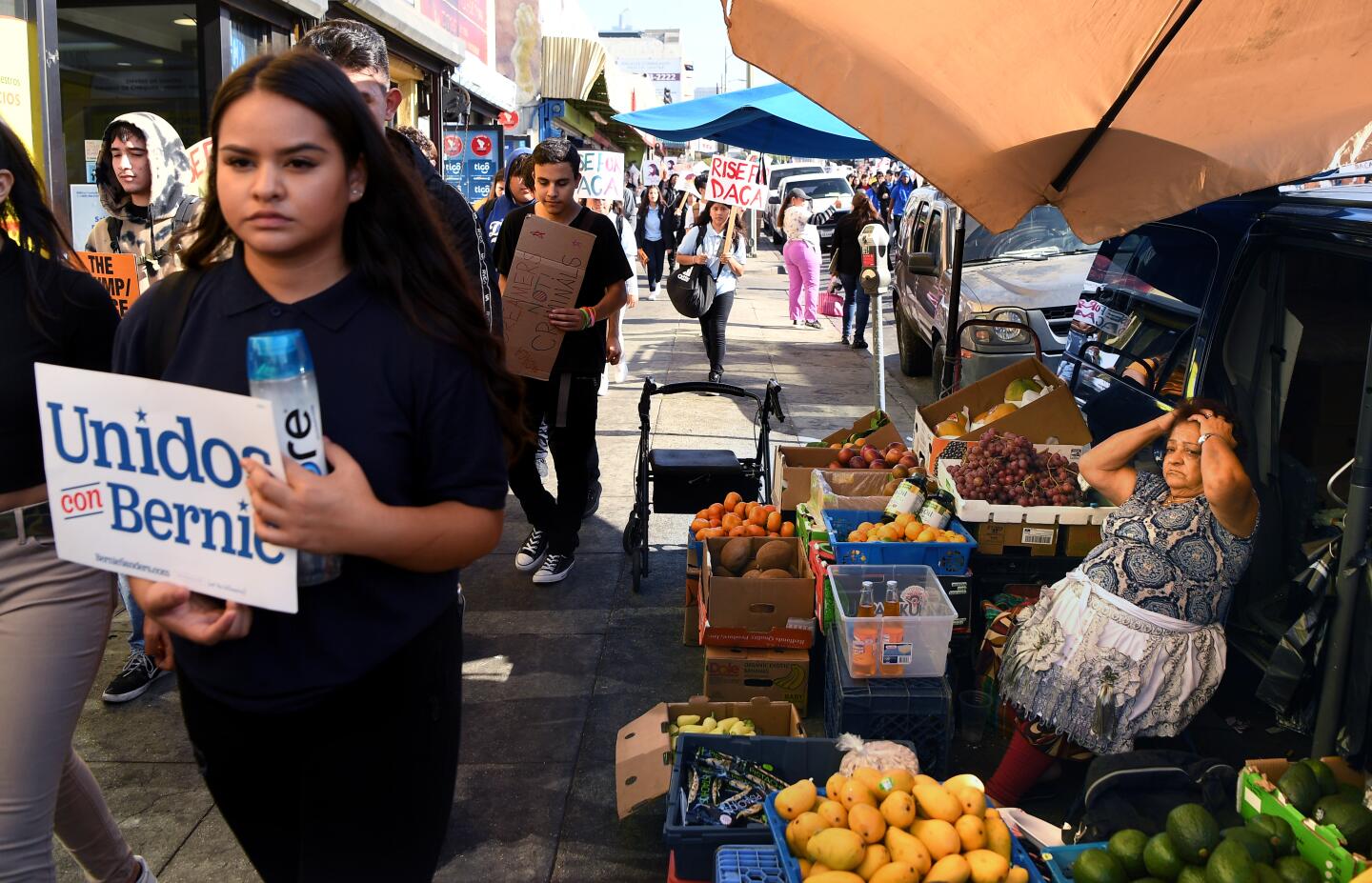 A street vendor selling fruit watches as DACA supporters march down 7th St. in Los Angeles .