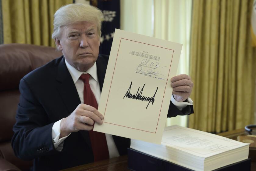 President Trump holds up a document during an event to sign the Tax Cut and Reform Bill in the Oval Office at The White House in Washington, DC on December 22, 2017.