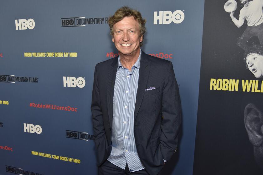 Nigel Lythgoe smiles and poses while wearing a dark blue suit jacket and a light blue dress shirt