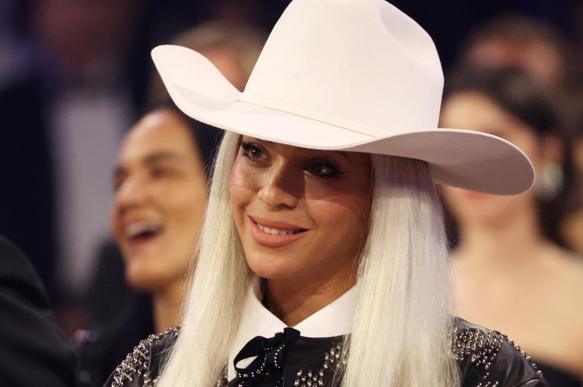 Beyonce wears a white cowboy hat and smiles in an audience