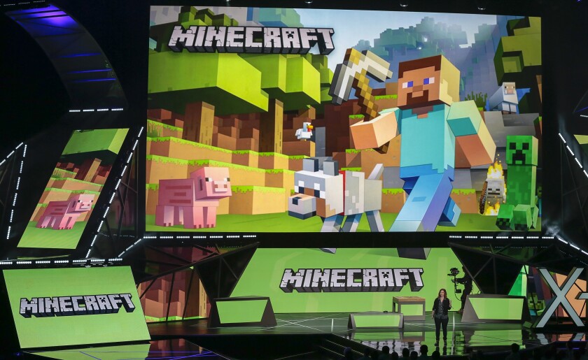 A woman presents "Minecraft" on a large screen onstage. 