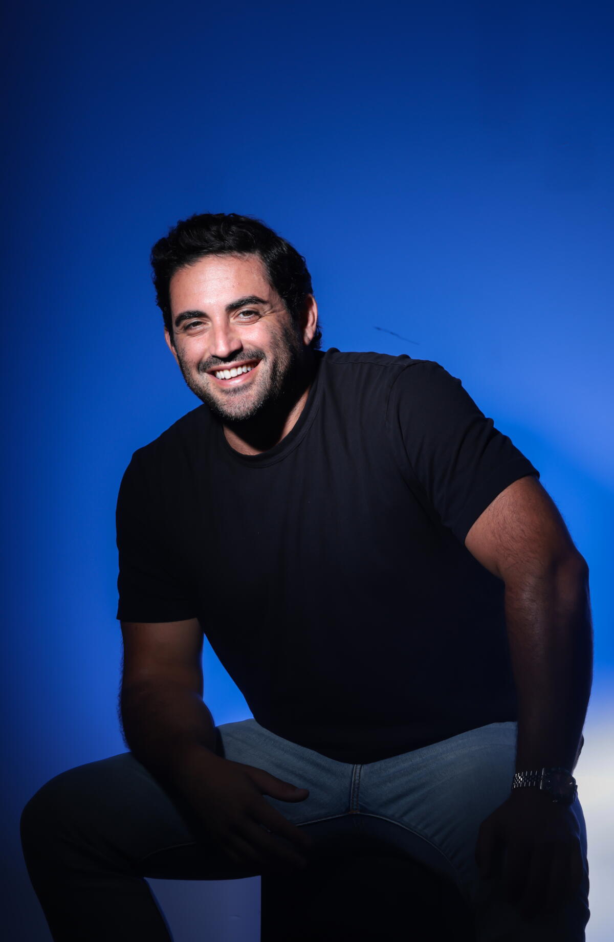 Comedian Jared Freid sitting in a stool against a blue background