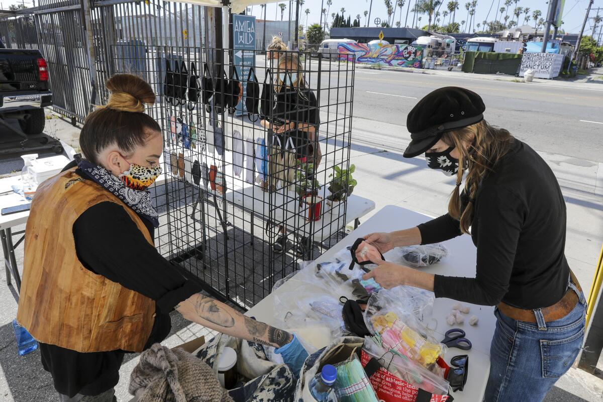 Sadie Gilliam, left, and Alisun Franson sell face masks from a stand in front of their store in Venice.