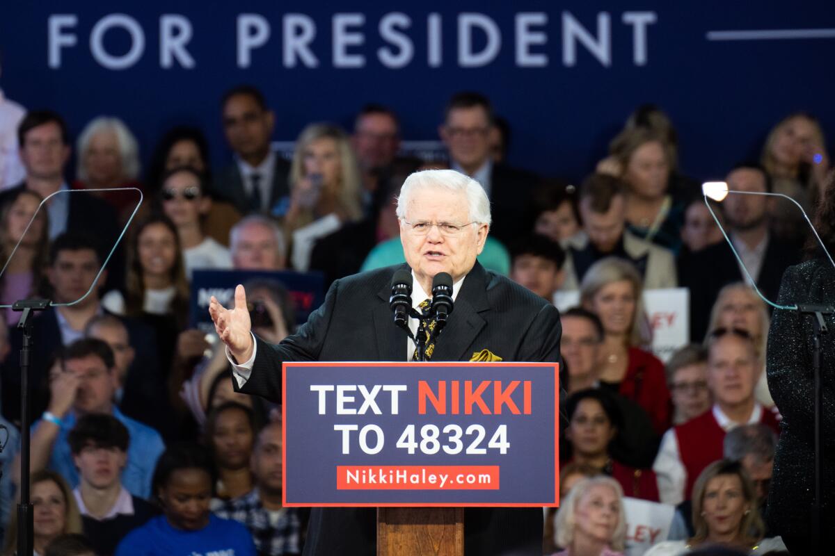 Pastor John Hagee gestures with his right hand as he speaks, standing behind a lectern  