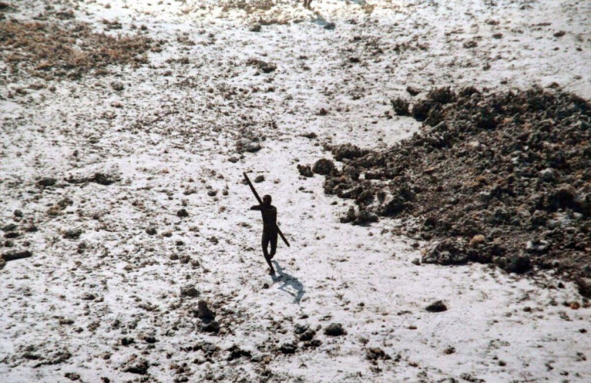 In a photo provided by the Indian Coast Guard and Survival International, a Sentinelese tribe member takes aim with bow and arrow at an Indian Coast Guard helicopter as it flies over North Sentinel Island in December 2004.