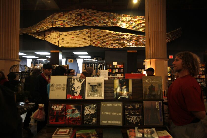 Visitors make their way through the Last Bookstore, which features a piece of art made of paperback books, background.