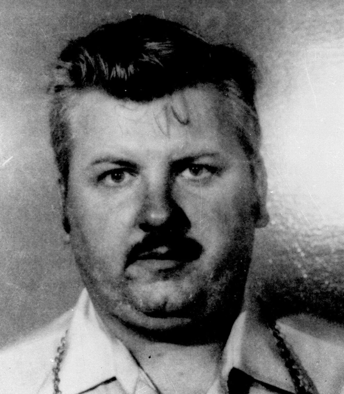 A black-and-white mug shot of a man with a mustache