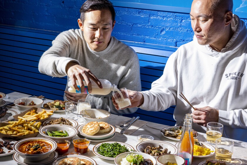 Two men sit at a table filled with food.