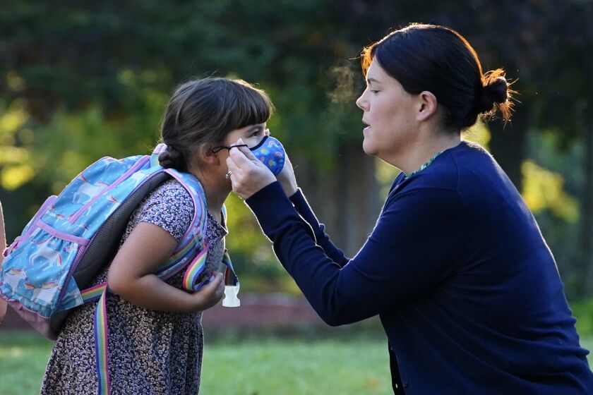 Sarah Staffiere adjusts a face covering on her daughter, Natalie, before school, Thursday, Oct. 7, 20211, in Waterville, Maine. Staffiere, a senior laboratory instructor at Colby College, said she will be relieved when her two children can be vaccinated. (AP Photo/Robert F. Bukaty)