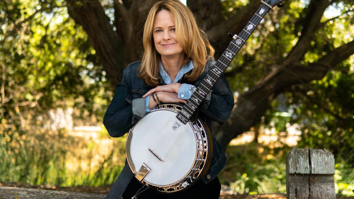 Alison Brown poses with a banjo under a tree.  