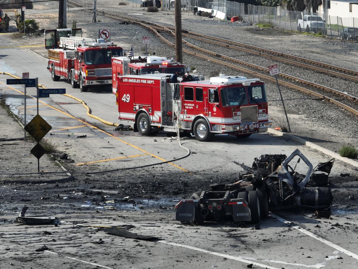 Two firetrucks are parked near a burned-out vehicle.