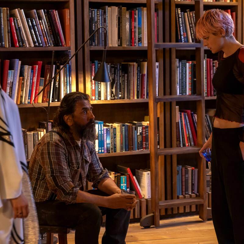 A man with a beard is flanked by two women in a library.
