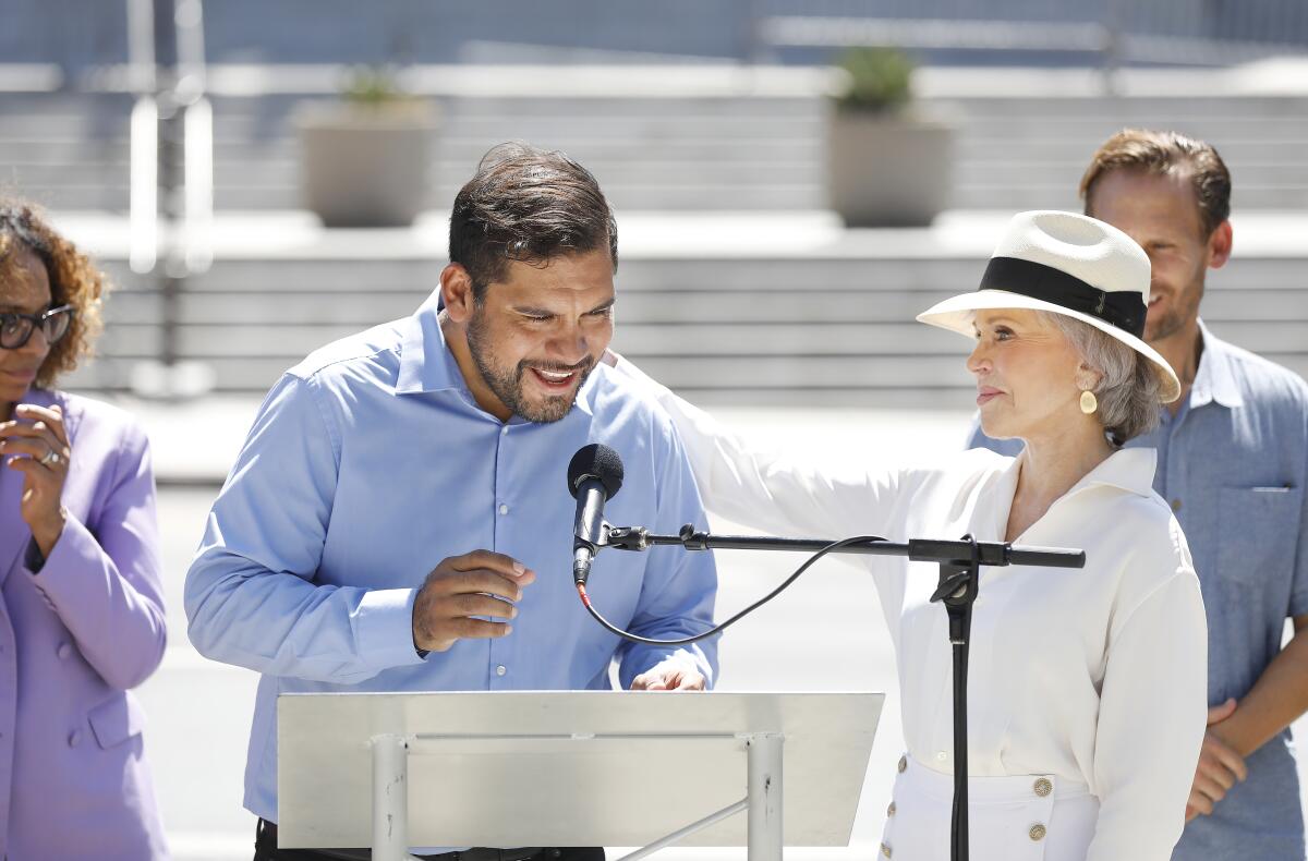 Hugo Soto-Martinez, left, speaks before a microphone next to actress Jane Fonda, right, outside City Hall.