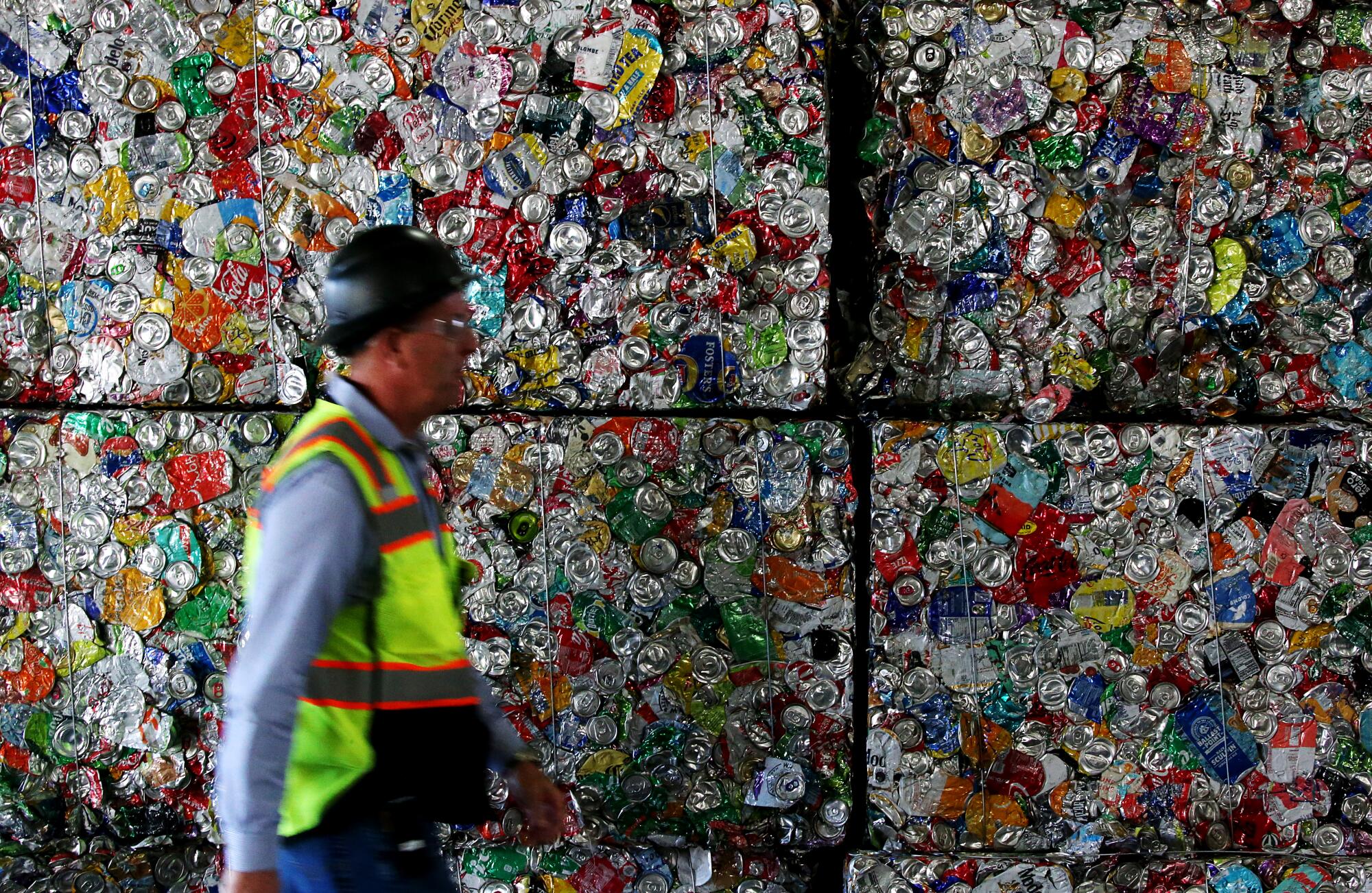 A worker walks past large blocks of crushed aluminum cans.