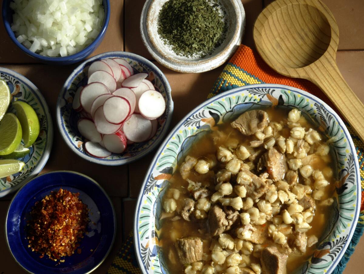 Posole Estilo Jalisco (Rojo) in a bowl with bowls of crushed chiles, lime, radishes, onion, oregano. 