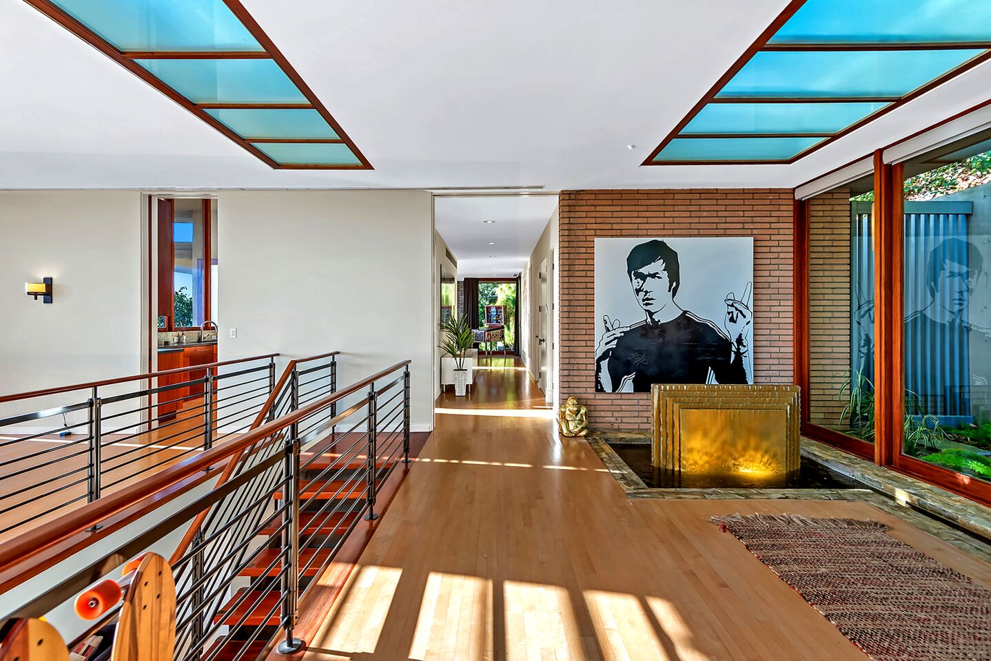 An open space has large windows, a brick wall with artwork of Bruce Lee and staircase to a lower floor.