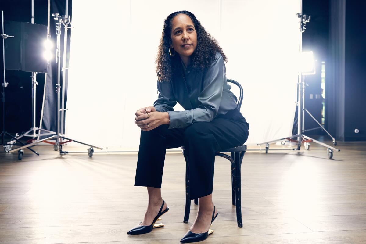 A woman sits leaning forward on a chair in front of a white backdrop