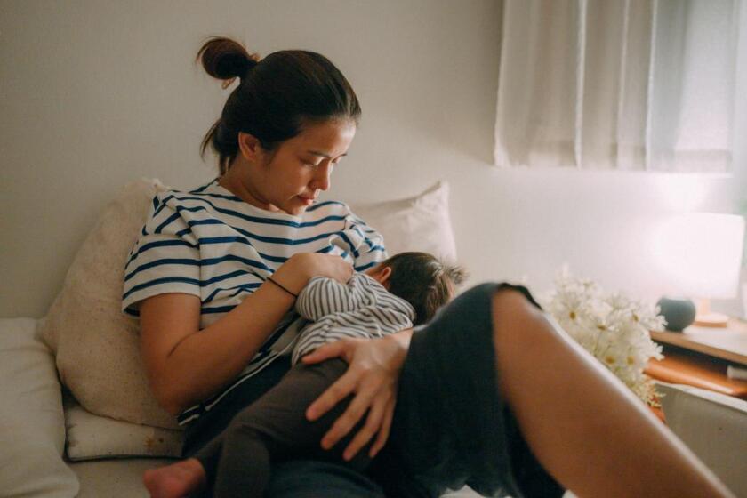 A woman breastfeeds her baby at home.