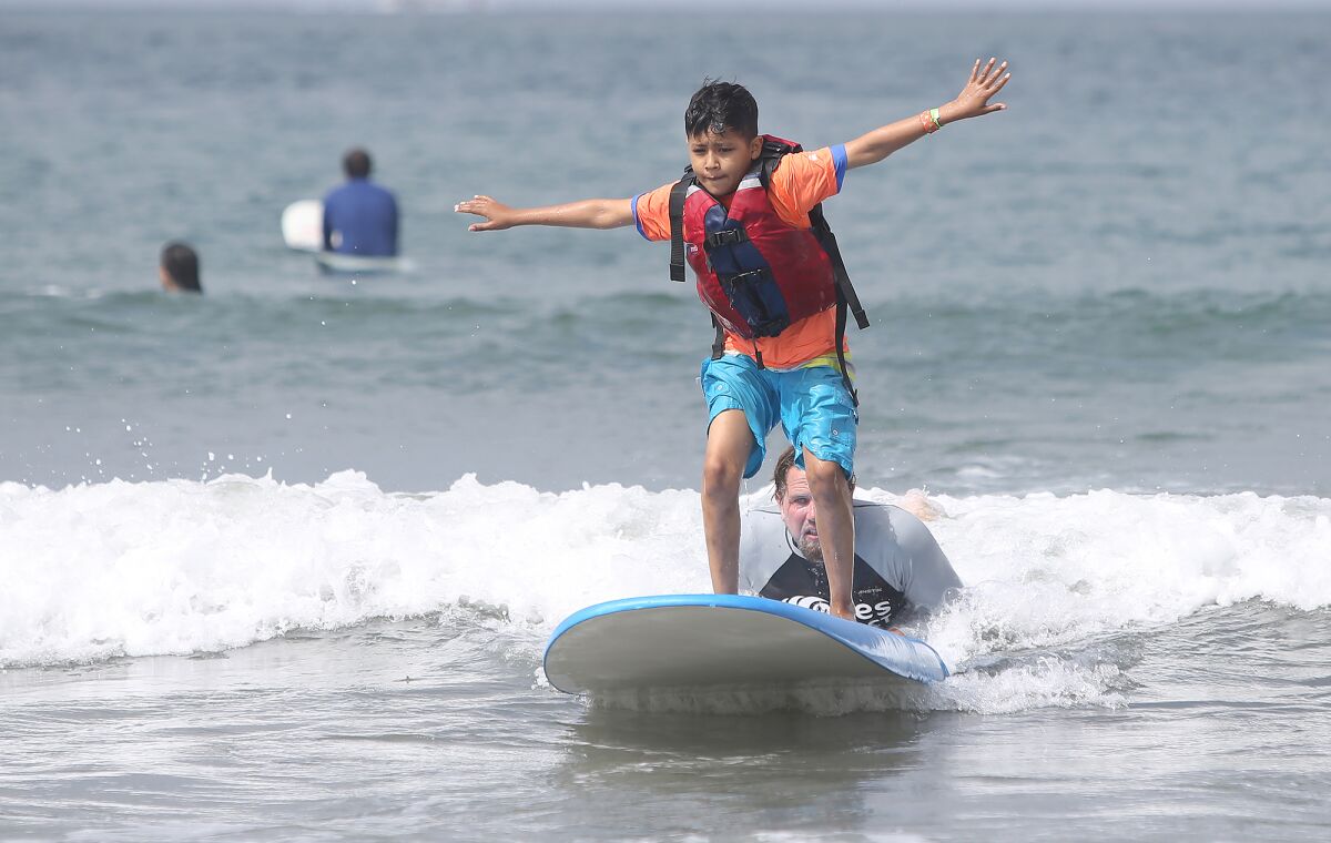 Kenneth Avendano gets to his feet and holds his balance while instructor Joe Iredell keeps him steady on the board as they participate in the Miracles for Kids surf camp Friday in Newport Beach.