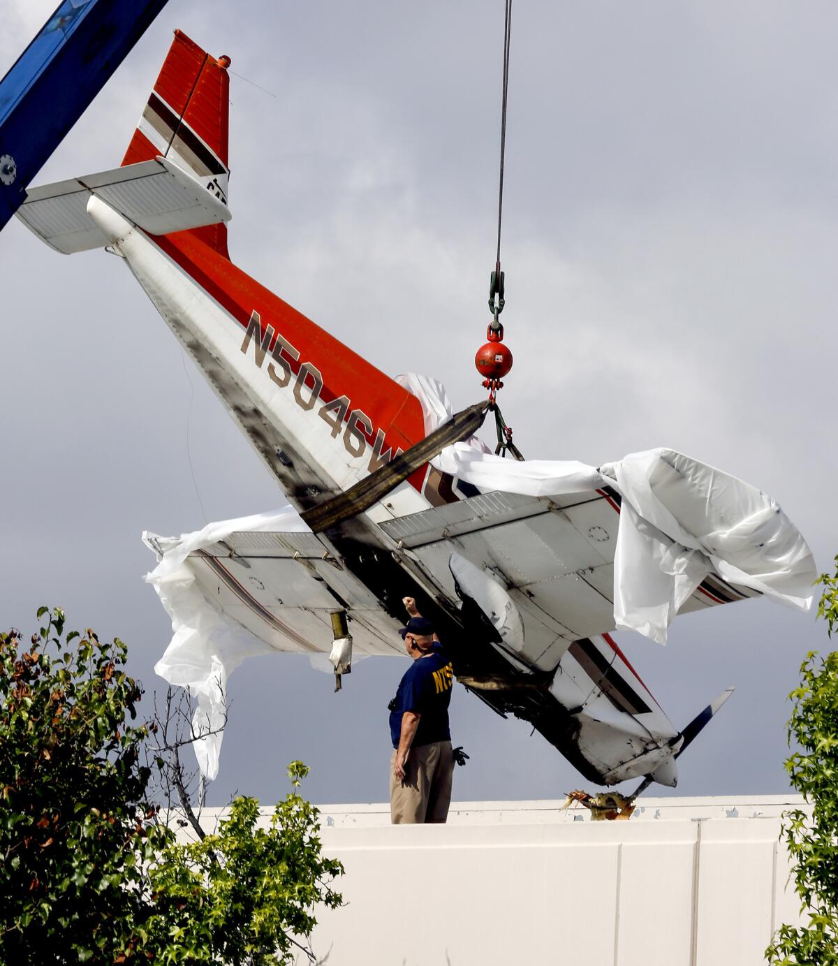 An agent with the National Transportation Safety Board guides a crane operator during the removal of a Piper PA-28 Cherokee from the roof of a building in Pomona on Monday.