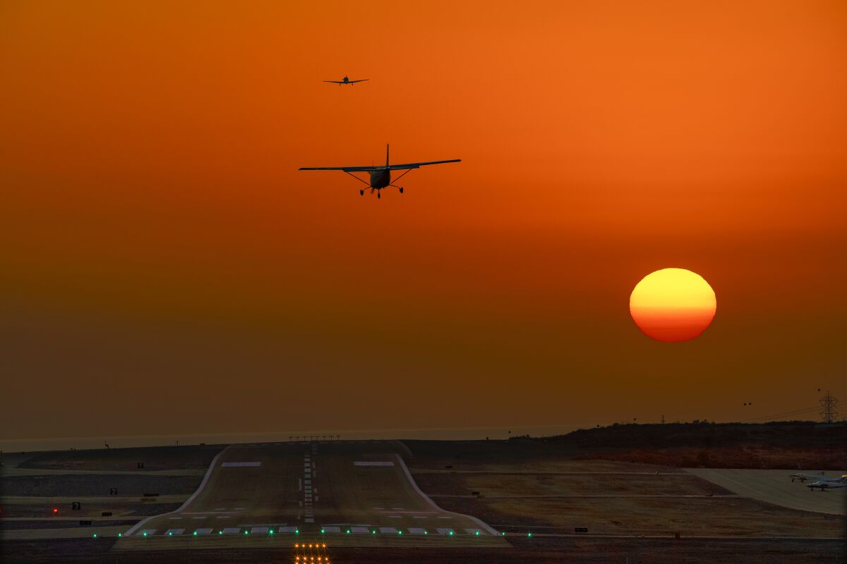 Two small planes fly above the runway at McClellan-Palomar Airport in Carlsbad during an October sunset.