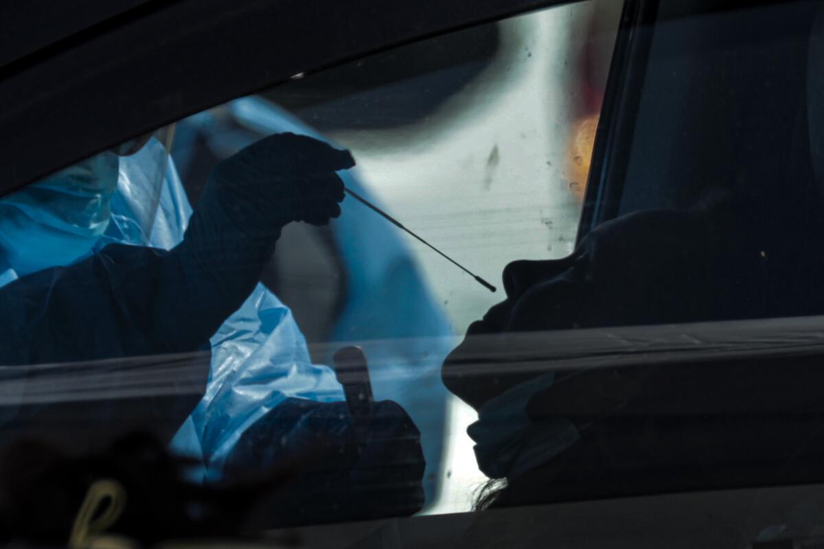 A worker takes a sample at a drive-through testing site in Victorville.