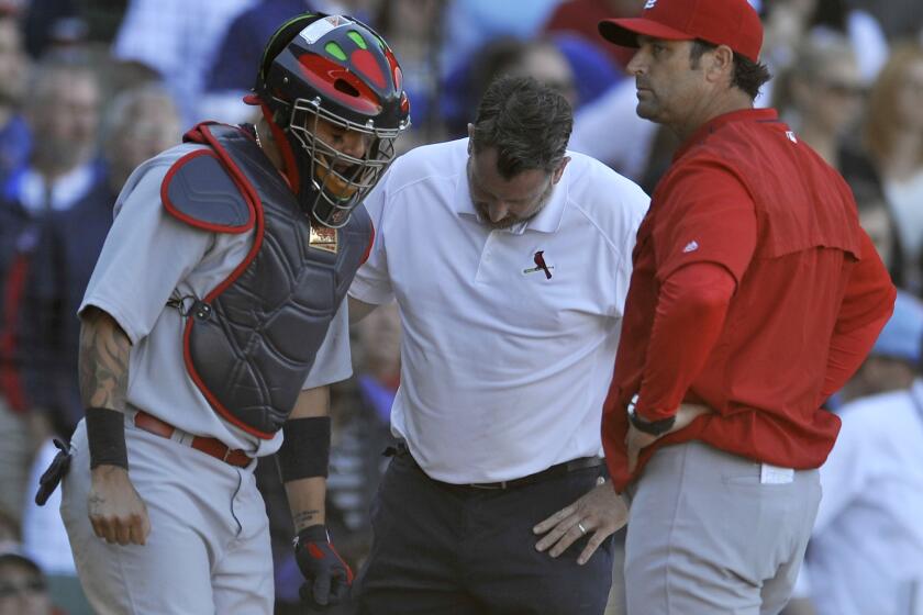 Cardinals catcher Yadier Molina is examined by a trainer after injuring his thumb while tagging out Cubs' runner Anthony Rizzo at home plate.