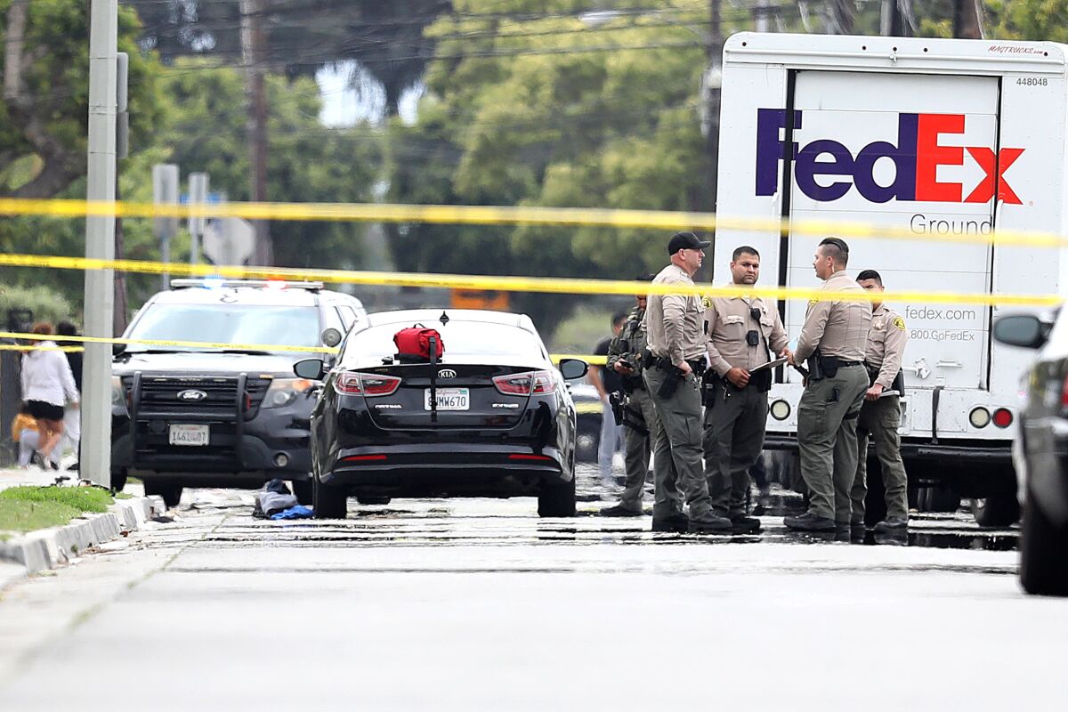 Sheriff's deputies on a street with parked vehicles and yellow police tape